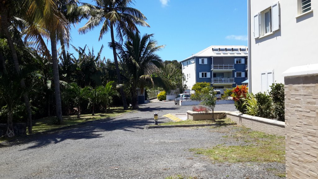 Extérieur de l'appartement côté parking (2 emplacements) avec fenêtre d'une chambre au rez de chaussée. Au fond le 2e bâtiment de la résidence avec 6 appartements également